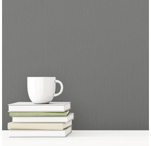 Graue Vliestapete mit Textilstruktur neben einer Tasse und Büchern