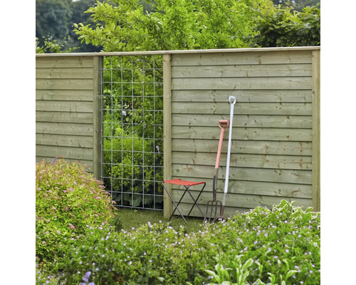Gartenansicht mit Holzzaun, Rankgitter, Gartengeräten und Gartenhocker