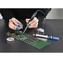 Person lötet mit Lötkolben, Lötzinn und Entlötpumpe eine Platine.