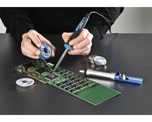 Person lötet mit Lötkolben, Lötzinn und Entlötpumpe eine Platine.