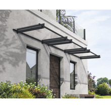 Modernes Vordach mit dunklem Metallrahmen und transparenten Paneelen über Haustür und Fenstern an einer grauen Steinfassade.