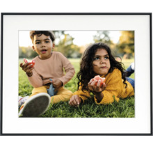 Schwarzer Bilderrahmen mit weißem Passepartout und einem Foto von zwei Kindern auf einer Wiese.
