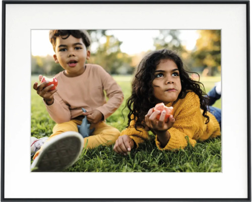 Schwarzer Bilderrahmen mit weißem Passepartout und einem Foto von zwei Kindern auf einer Wiese.