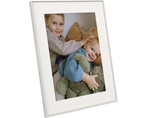 Weißer Bilderrahmen mit Passepartout, schräg dargestellt, zeigt ein Foto von zwei lachenden Kindern mit einem Teddybären.