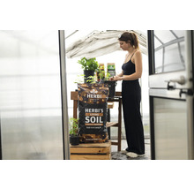 Ein Sack Herbi's Living Soil in einem Gewächshaus mit einer Frau im Hintergrund.