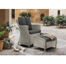 Geflochtener Sessel mit Fußhocker und grauen Polstern auf einer gepflasterten Terrasse.