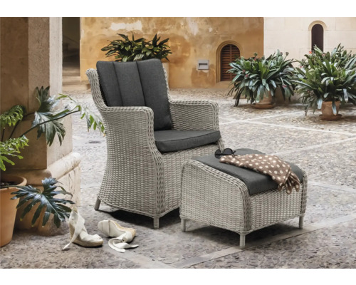 Geflochtener Sessel mit Fußhocker und grauen Polstern auf einer gepflasterten Terrasse.