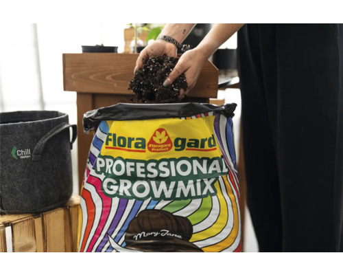 Eine Person schaufelt Blumenerde aus einem Sack Floragard Professional Growmix. Daneben steht ein grauer Pflanzbehälter.