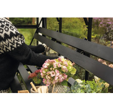 Detailansicht einer schwarzen Gewächshausbank mit Blumen und einer Person im Hintergrund