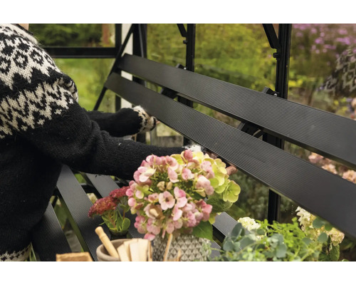 Detailansicht einer schwarzen Gewächshausbank mit Blumen und einer Person im Hintergrund