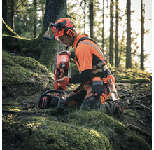 Ein Waldarbeiter kniet im Wald mit einer Motorsäge und einem Treibstoffkanister, er trägt Schutzkleidung.