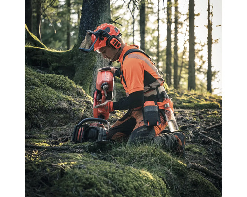 Ein Waldarbeiter kniet im Wald mit einer Motorsäge und einem Treibstoffkanister, er trägt Schutzkleidung.