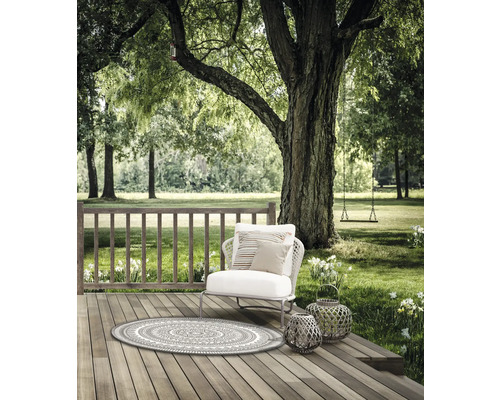 Szene im Garten mit Gartenteppich, Sessel, Kissen und Laternen auf einer Holzterrasse