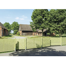 Moderner Sichtschutzzaun aus Holz mit waagerechten Lamellen vor einem ländlichen Anwesen mit Scheune und großen Bäumen.