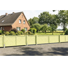 Hellgrüner Gartenzaun aus Holz mit diagonal angeordneten Lamellen vor einem Backsteinhaus mit weitläufigem Garten.