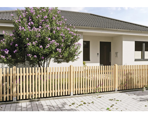Vorgartenzaun als Lattenzaun aus Holz vor einem modernen Wohnhaus mit einem blühenden Strauch auf einem gepflasterten Grundstück.