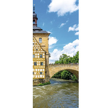 Historisches Fachwerkhaus an einem Fluss mit einer steinernen Bogenbrücke unter blauem Himmel.