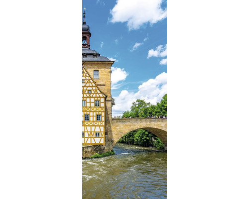Historisches Fachwerkhaus an einem Fluss mit einer steinernen Bogenbrücke unter blauem Himmel.