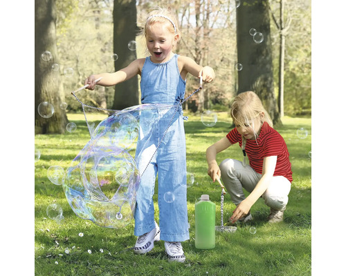 Zwei Kinder spielen im Park mit einem Seifenblasenset und erzeugen große Seifenblasen.