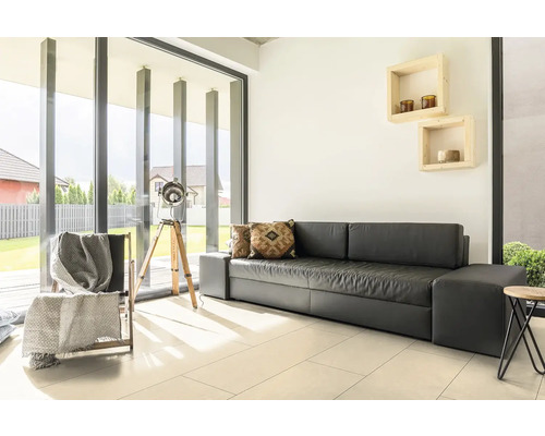 Modernes, helles Wohnzimmer mit dunklem Sofa, hellen Bodenfliesen und großen Fensterfronten zum Garten.