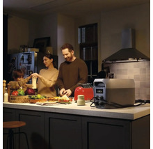 Tragbare Powerstation auf einer Kücheninsel, die einen Toaster mit Strom versorgt, während eine Familie in einer modernen Küche Essen zubereitet.