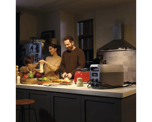 Tragbare Powerstation auf einer Kücheninsel, die einen Toaster mit Strom versorgt, während eine Familie in einer modernen Küche Essen zubereitet.