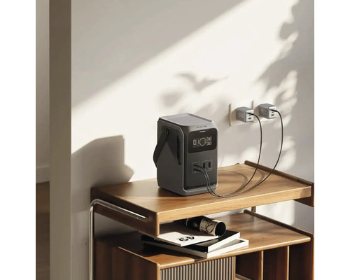 Tragbare Powerstation auf einem Regal, angeschlossen an eine Wandsteckdose mit zwei USB-Kabeln.
