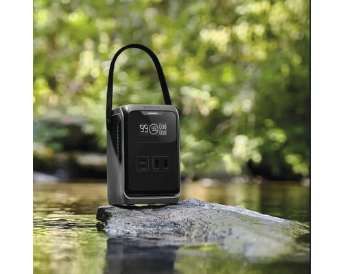 Tragbare Powerstation mit Tragegriff und digitalem Display auf einem Stein in einem Bach vor einem unscharfen Waldhintergrund.
