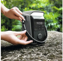 EcoFlow tragbare Powerstation mit digitalem Display und verschiedenen Anschlüssen im Außenbereich. Eine Person befestigt einen Tragegurt am Gerät.