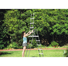 Eine Frau baut eine graue Poolleiter mit weißen Stufen auf einer Rasenfläche in einem hellen, weitläufigen Garten auf.