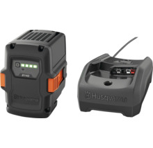Husqvarna Akku B140 und Ladegerät. Der schwarze Akku besitzt orangefarbene Entriegelungstasten und eine Ladestandsanzeige. Husqvarna Logo.