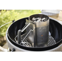 Anzündkamin aus Metall gefüllt mit Grillkohle auf einem Grillrost in einem Kugelgrill im Freien.