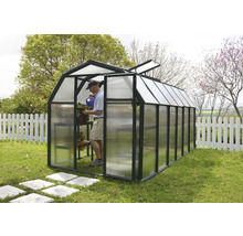 Gewächshaus mit schwarzem Rahmen und lichtdurchlässigen Paneelen im Garten. Ein Mann gießt Pflanzen in der hellen Struktur.