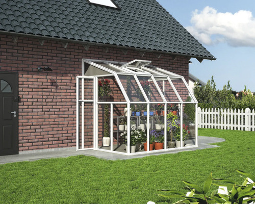 Anlehngewächshaus aus weißem Aluminium und Glas mit Dachfenster, montiert an einer Ziegelwand im Garten.