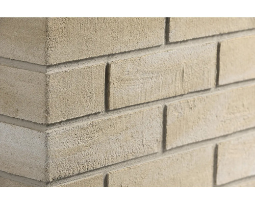 Nahaufnahme einer Mauer aus beigen Verblendsteinen mit rauer Textur und grauen Mörtelfugen an einer Hausecke.