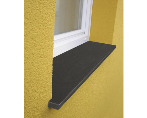 Außenfensterbank aus dunklem Stein unter einem weißen Fensterrahmen an einer verputzten Fassade.