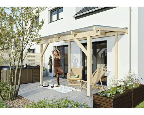 Moderne Terrassenüberdachung aus hellem Holz an einer Hauswand, davor eine gepflasterte Terrasse mit Gartenmöbeln und Whirlpool.