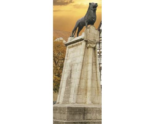 Braunschweiger Löwe Bronzestatue auf einem hohen Steinsockel vor historischer Kulisse mit herbstlichen Bäumen.