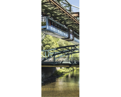 Wuppertaler Schwebebahn fährt über einem Fluss unter einer Stahlkonstruktion mit Bäumen im Hintergrund.