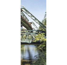 Industrielle Stahlkonstruktion der Wuppertaler Schwebebahn über einem Fluss mit Uferbepflanzung und Fußgängersteg.
