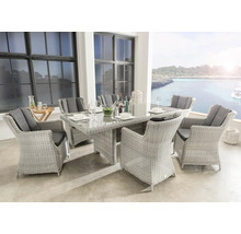 Gartenmöbel-Set aus hellem Polyrattan mit Glastisch und sechs Sesseln inklusive dunkler Kissen auf einer hellen Terrasse mit Meerblick.