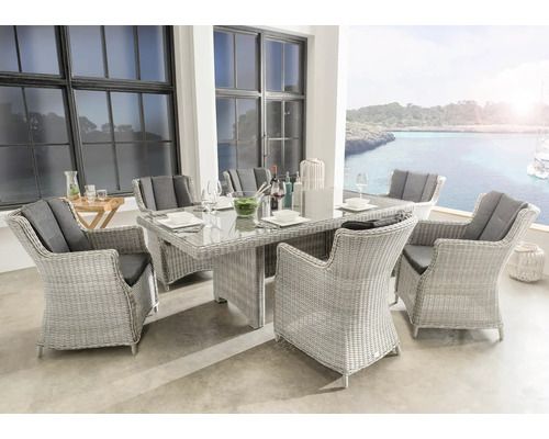 Gartenmöbel-Set aus hellem Polyrattan mit Glastisch und sechs Sesseln inklusive dunkler Kissen auf einer hellen Terrasse mit Meerblick.