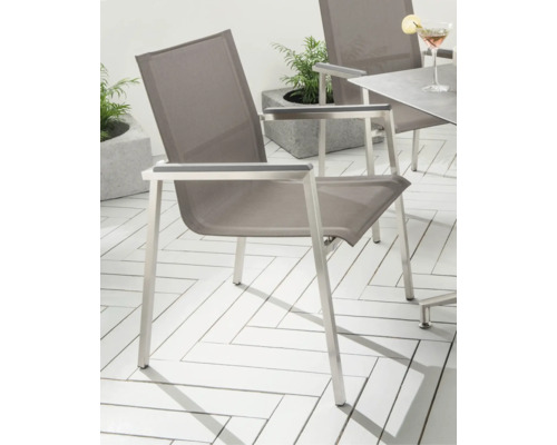 Moderner Gartenstuhl mit silberfarbenem Metallgestell und grauem Textilgewebe auf einer hellen Terrasse mit Fischgrätmuster.