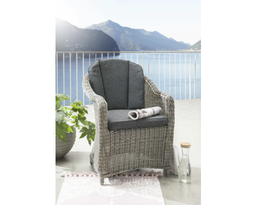 Geflochtener Gartenstuhl mit grauen Sitz- und Rückenpolstern auf einem hellen Balkon mit Aussicht auf See und Berge.