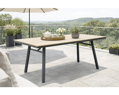 Moderner Gartentisch mit Tischplatte in Holzoptik und dunklem Metallgestell auf einer Terrasse mit Pflanzen und Landschaftsblick.