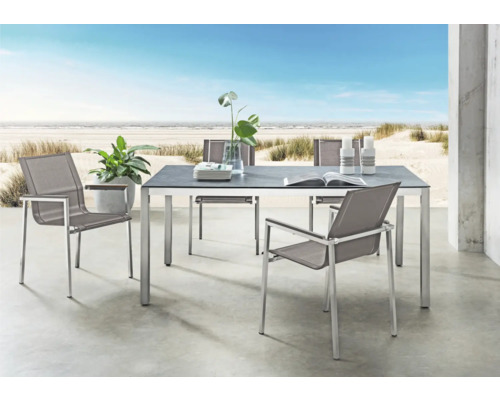 Moderne Gartenmöbelgruppe mit rechteckigem Esstisch und vier Stühlen auf einer Terrasse mit Strandblick. Tisch mit dunkler Platte und Metallgestell.