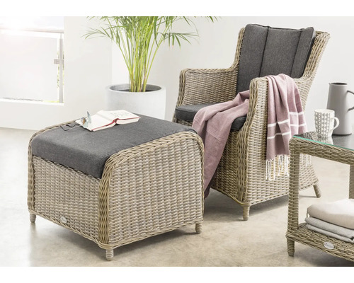 Modernes Set aus Sessel, Hocker und Beistelltisch aus Geflecht mit Polstern in einem hellen, geräumigen Wohnbereich mit Zimmerpflanze.