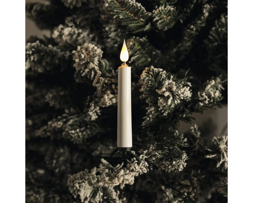 LED-Christbaumkerze an einem verschneiten Tannenbaumzweig mit warmweißem Licht.