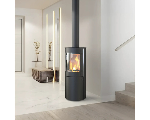 Moderner, zylindrischer Kaminofen aus schwarzem Stahl mit brennendem Feuer in einem hellen, minimalistischen Wohnraum.