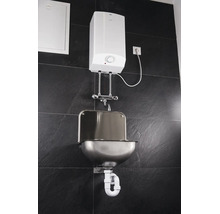 Wandmontierter AEG Warmwasserspeicher mit AEG Logo, verchromter Armatur, Edelstahl-Waschbecken und Siphon an einer Fliesenwand.